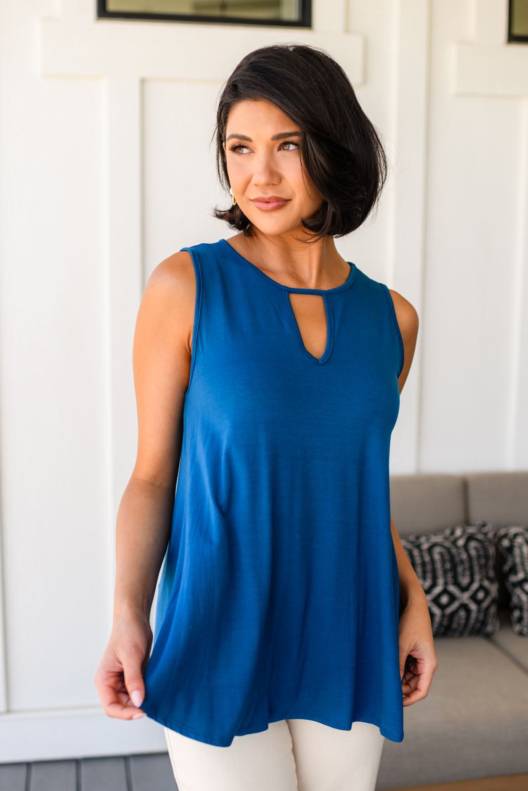 Woman wearing a blue sleeveless tank top with a cutout design, standing in a room with a white wall and gray couch
