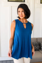 Woman wearing a blue sleeveless tank top with a cutout design, standing in a room with a white wall and gray couch