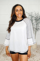A woman wearing a white and black striped sleeve top with a round neckline, made from French Terry fabric, paired with black shorts.