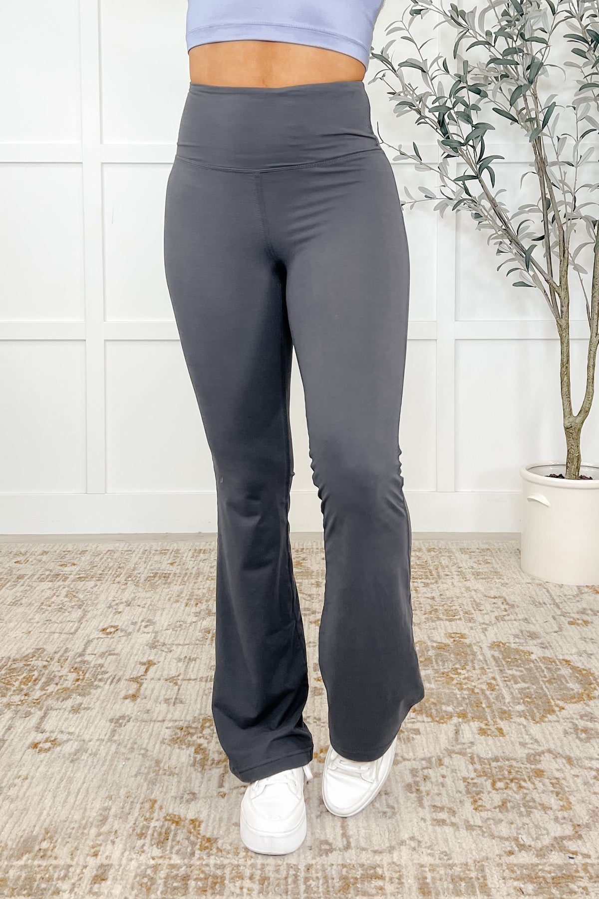 Woman wearing gray flared yoga pants with a high waisted design and banded waist.