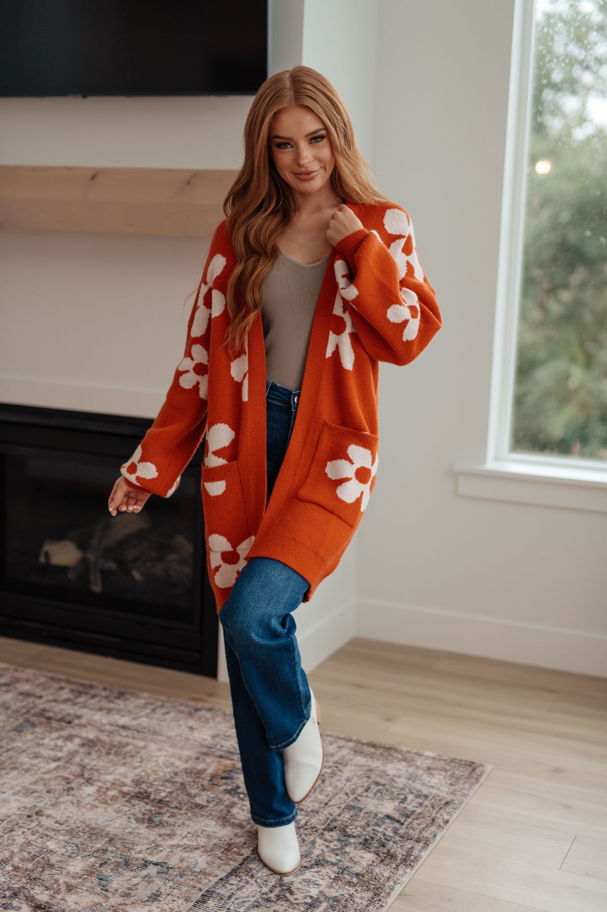 A woman wearing a burnt orange cardigan with large white floral patterns, open front, and balloon sleeves.