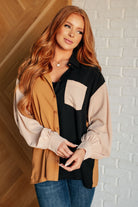 Woman wearing a color-blocked shirt against a white brick wall.