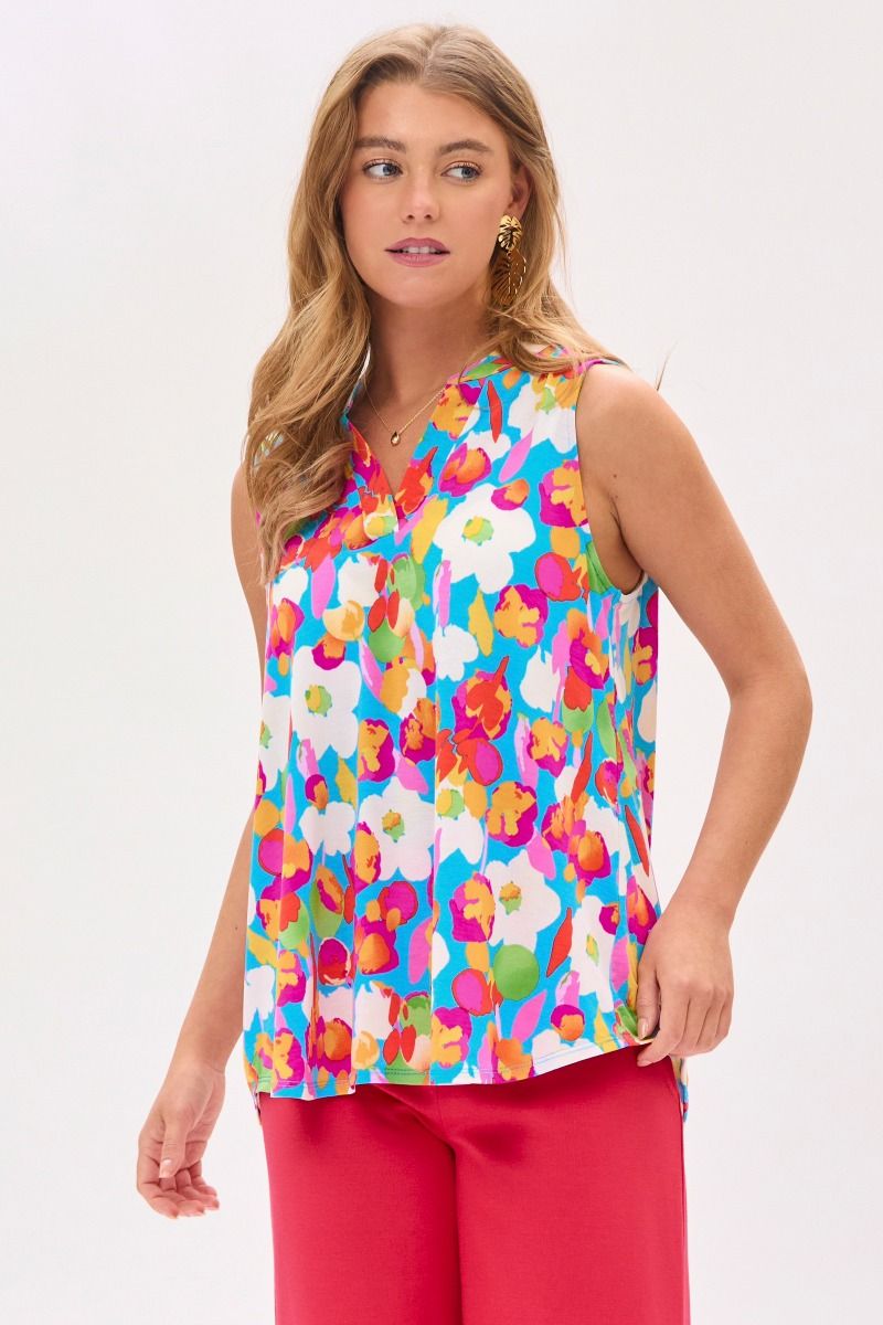 Woman wearing a colorful floral top and pink pants on a white background.