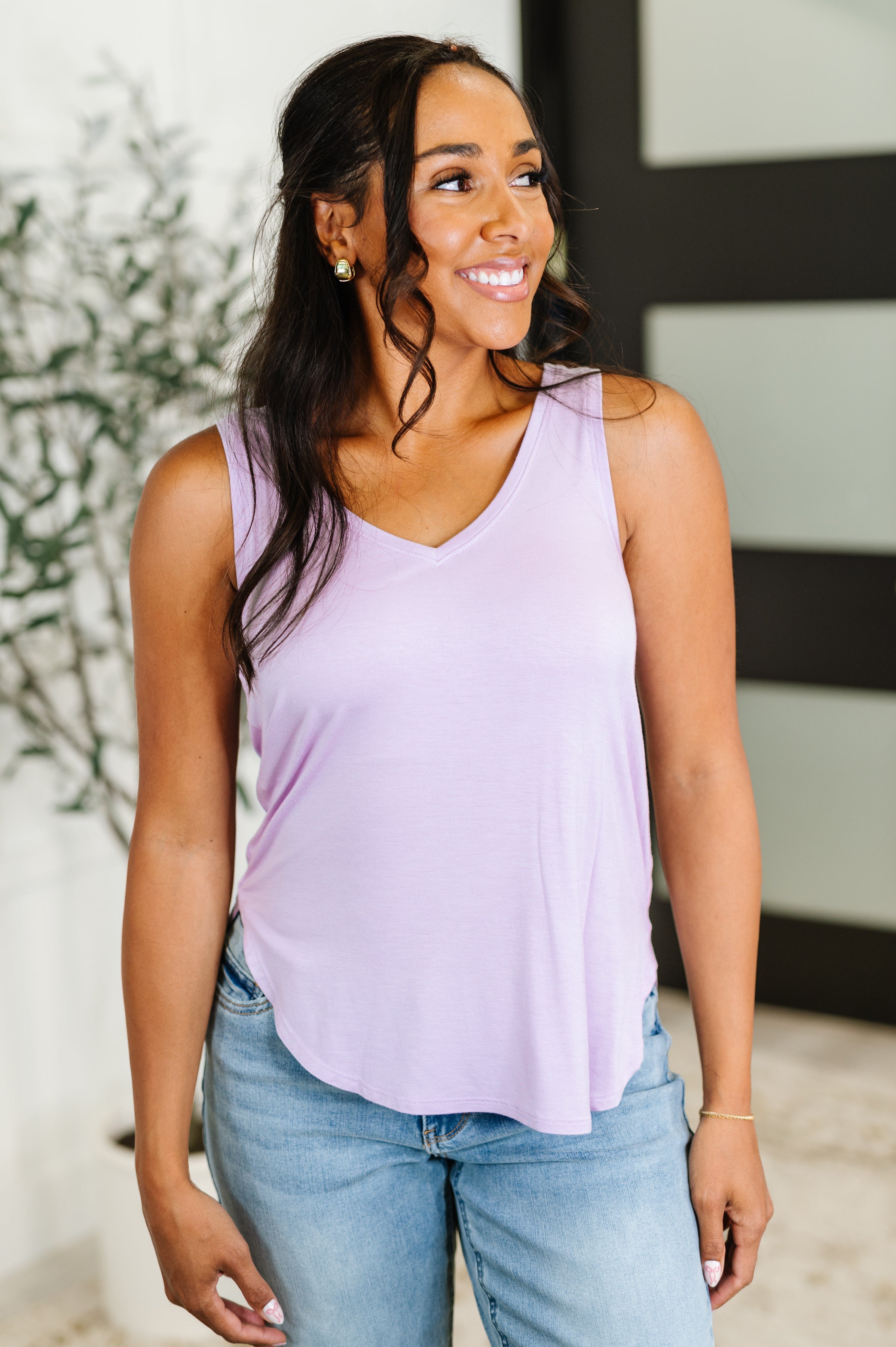 Woman wearing a light purple sleeveless top and blue jeans indoors.