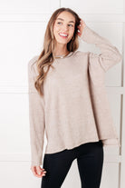 Woman wearing a beige mocha long-sleeve top and black pants against a white background