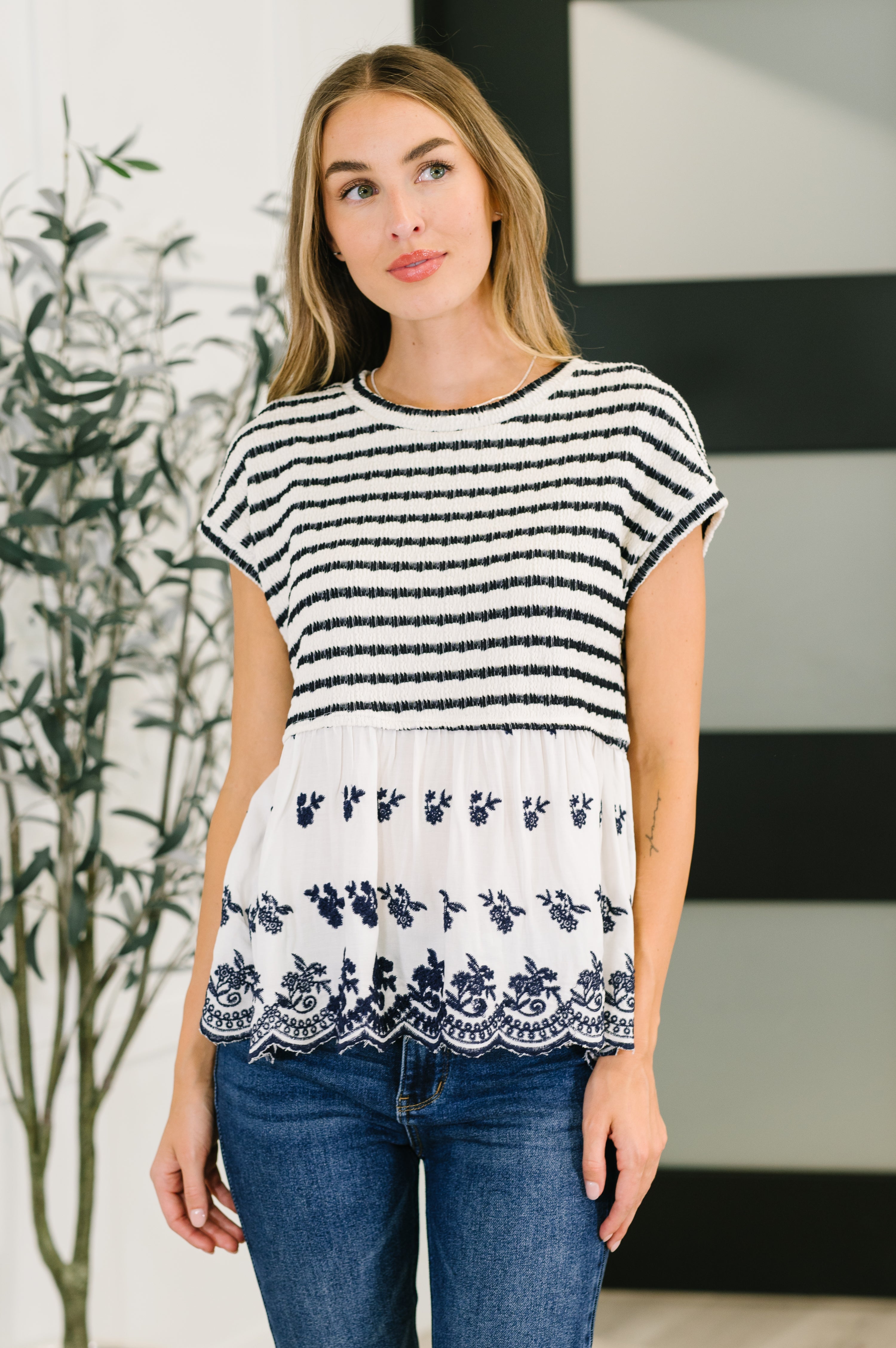 Woman wearing a black and white striped top with floral lace details, standing indoors.