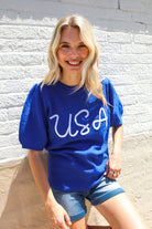 Woman wearing a blue 'USA' t-shirt against a light gray wall.