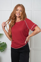 Woman wearing a red top with white trim against a white wall