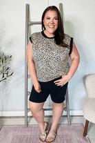 Woman wearing a leopard print top and black shorts standing in a room with a ladder and plant.