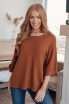 Woman wearing a brown sweater and blue jeans indoors