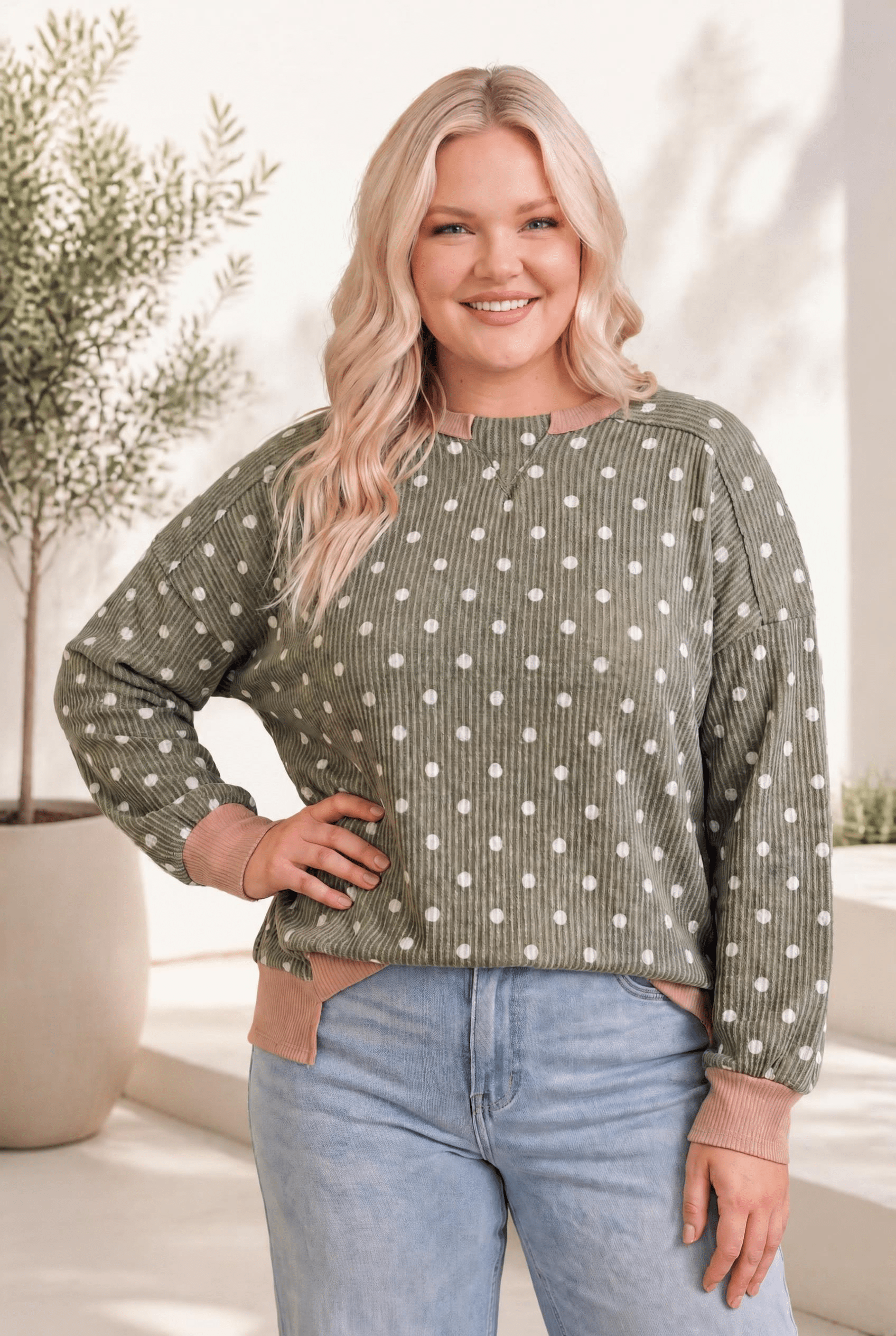A cozy ribbed pullover in olive with white polka dots, mauve trim, and a relaxed fit, worn by a smiling model.