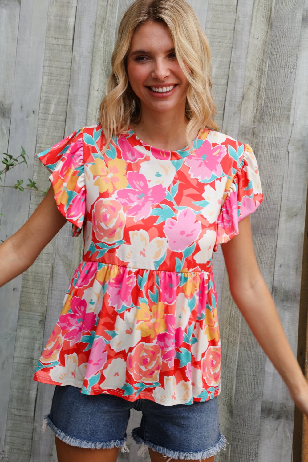 Woman wearing a colorful floral blouse with ruffled sleeves against a wooden background