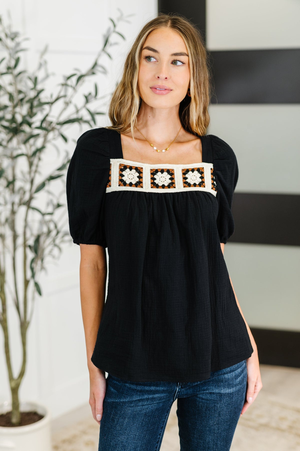 Woman wearing a black top with decorative embroidery in an indoor setting