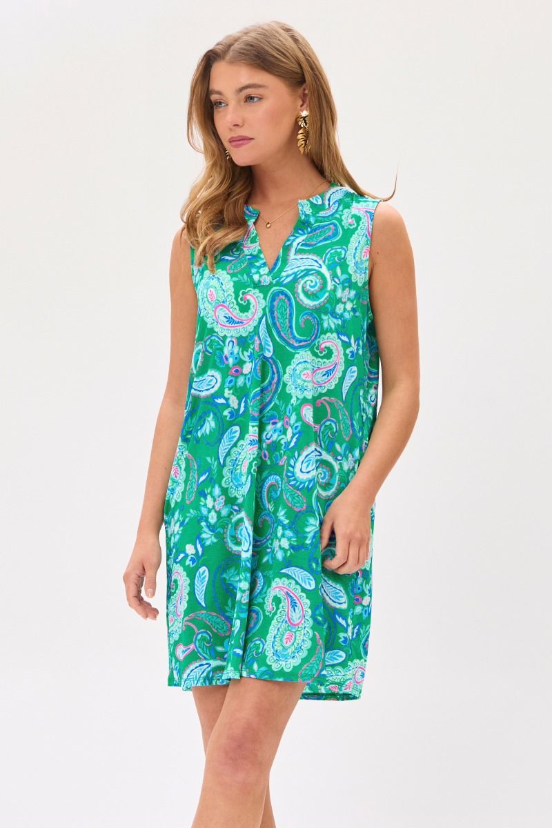 Woman wearing a sleeveless, emerald and blue floral print dress with a mandarin collar and pleated detail on the back.