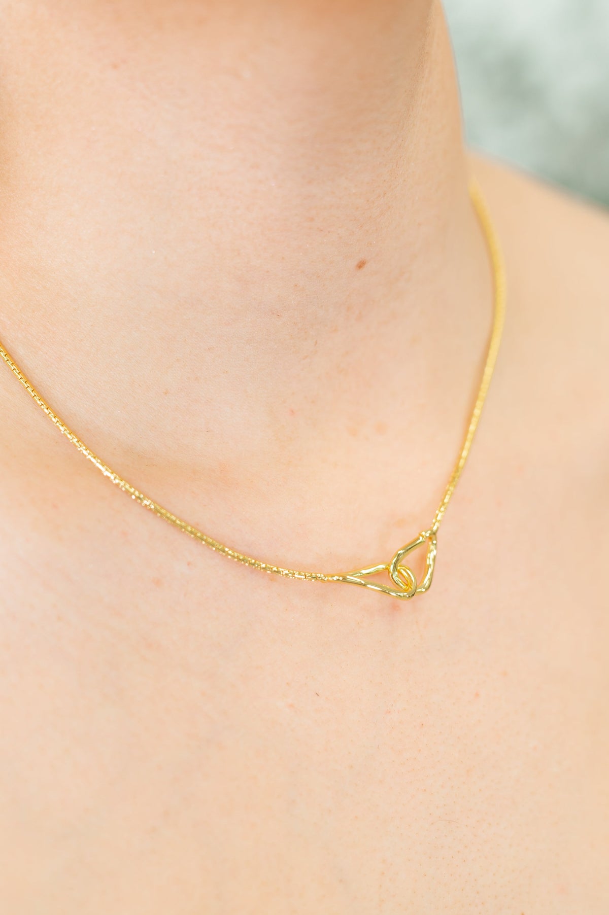 Gold necklace on a woman's neck against a neutral background