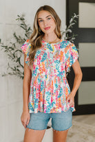 Woman wearing a colorful floral top and denim shorts indoors.