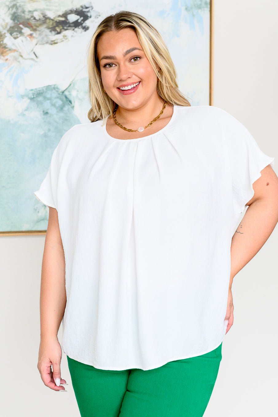 A woman wearing a white pleated detail top with dolman sleeves and green trousers.