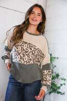 Woman wearing a patterned long-sleeve shirt against a white wall with greenery.