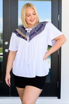 Woman wearing a white shirt with a colorful pattern in front of a glass door.