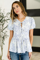 Woman wearing a white floral blouse with a blurred indoor background