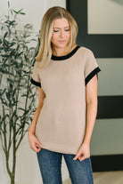 Woman wearing a beige sweater with black trim in an indoor setting