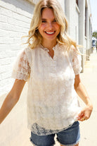A woman wearing an ivory Swiss dot chiffon button yoke lined blouse with short sleeves and denim shorts.