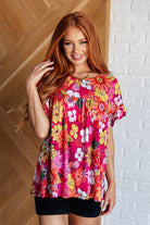 A woman wearing a pink floral top with a round neckline and short, flutter sleeves.