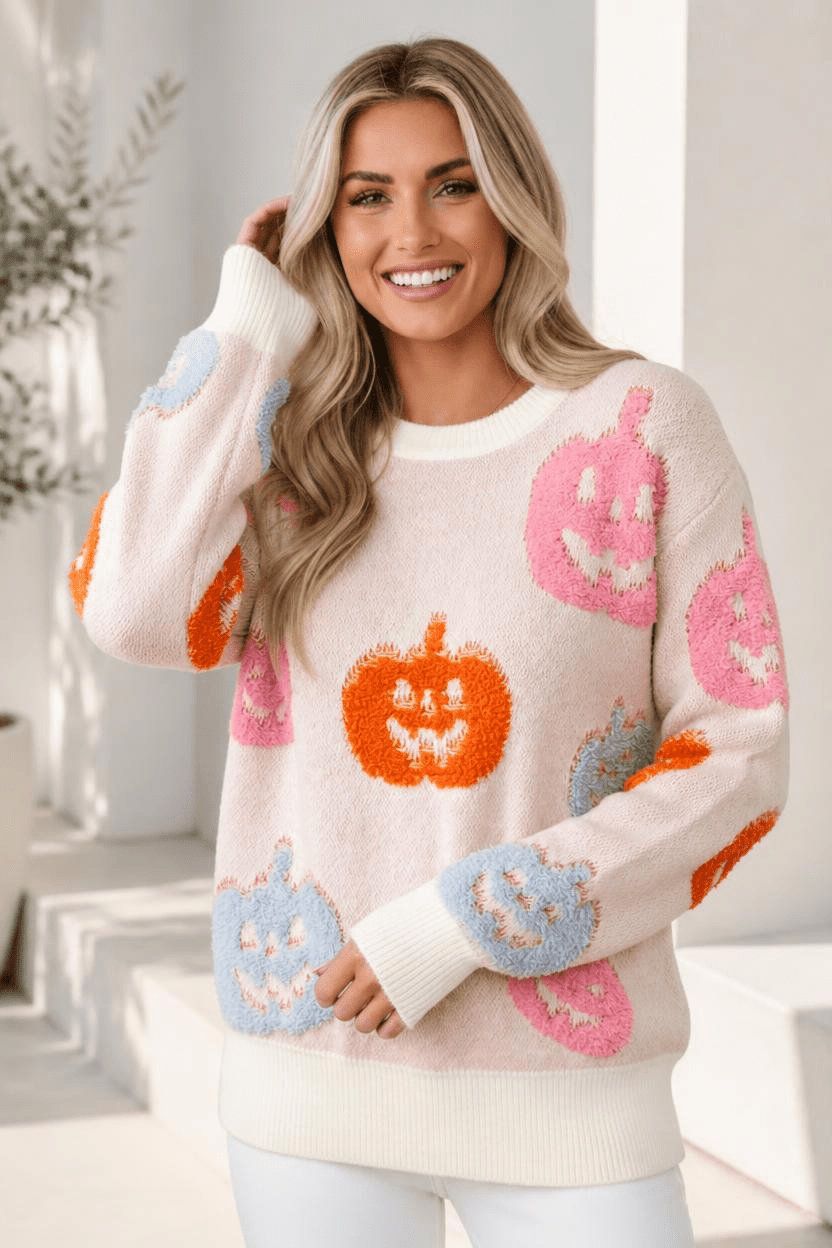 A pastel knit sweater with a jack-o'-lantern pattern and ribbed cuffs, worn by a smiling person.