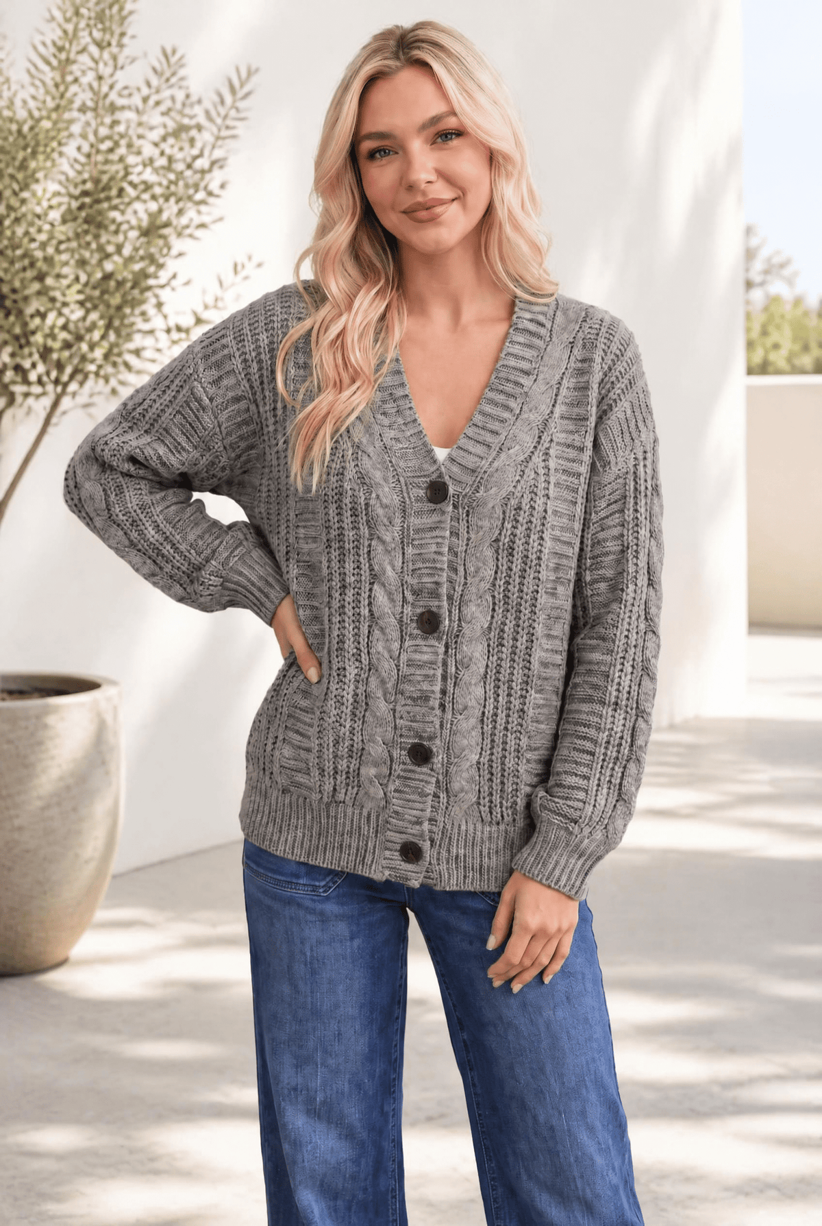 A woman wearing a chunky olive cable knit cardigan with dark buttons and a V-neckline, paired with jeans.