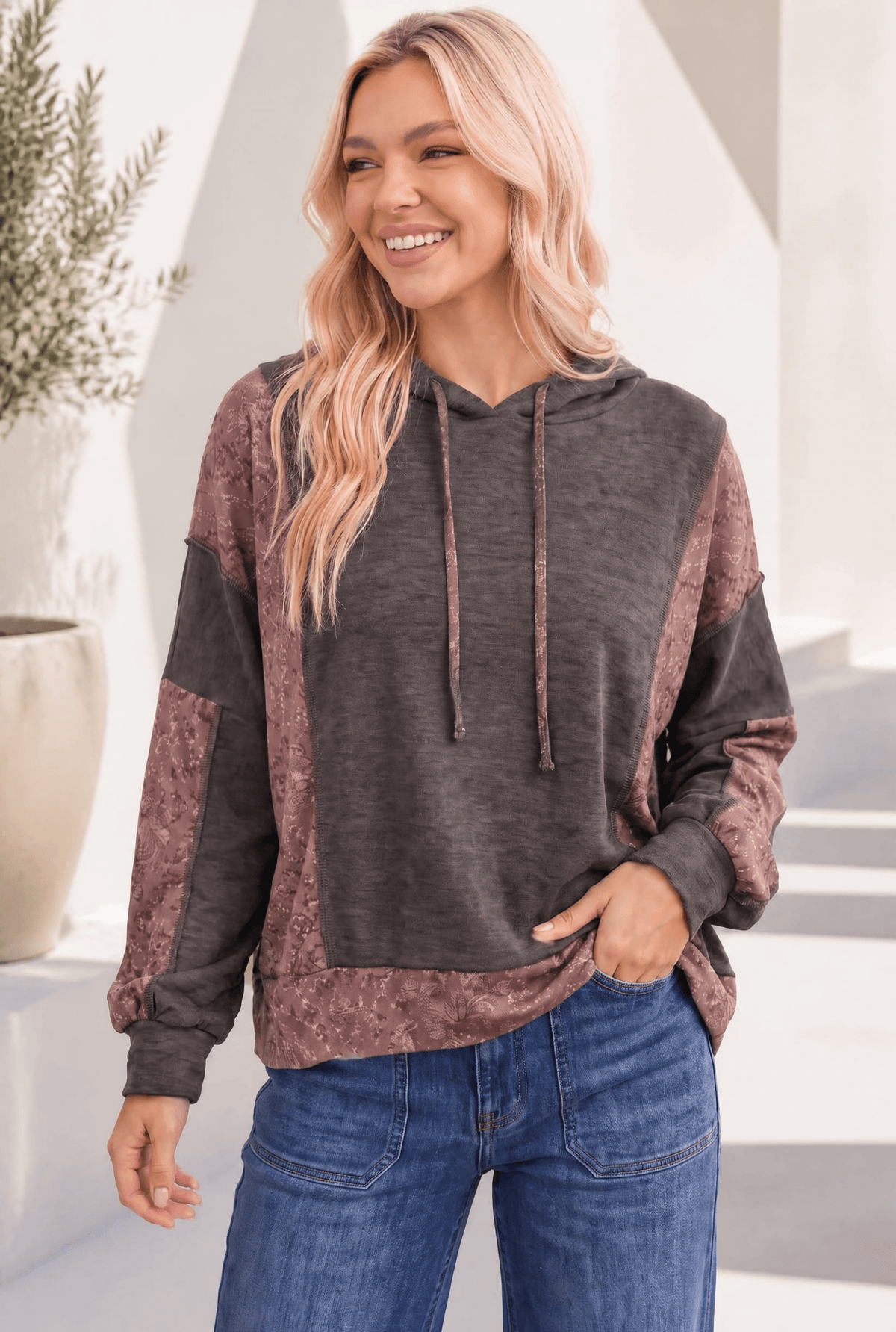 Woman wearing a brown patchwork hoodie with floral jacquard accents, featuring a drawstring hood and a kangaroo pocket.
