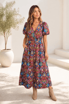 A woman wearing a chocolate brown midi dress with a colorful floral pattern and puff sleeves.