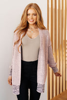 Woman wearing a long, patterned cardigan over a beige top and black pants, standing against a neutral background.