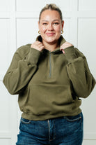 A woman wearing a green half zip pullover with a high neckline and kangaroo pocket.