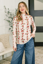 Woman wearing a high neck floral top with cable ribbed knit and lettuce hem, paired with wide-leg jeans.
