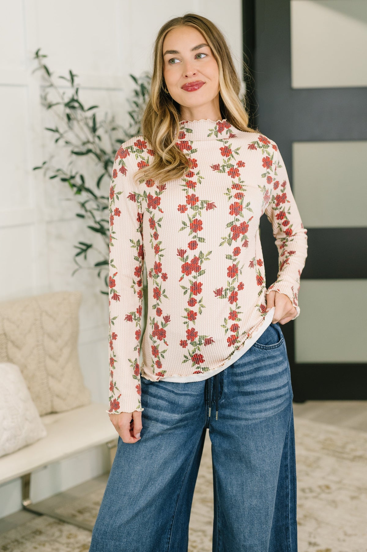 Woman wearing a high neck floral top with cable ribbed knit and lettuce hem, paired with wide-leg jeans.