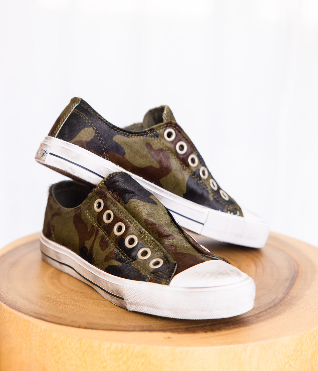 A pair of sneakers with a camouflage pattern on a cowhide upper with white distressed accents and elastic tongues.